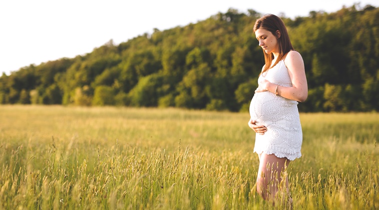 Pregnant woman holding belly in nature